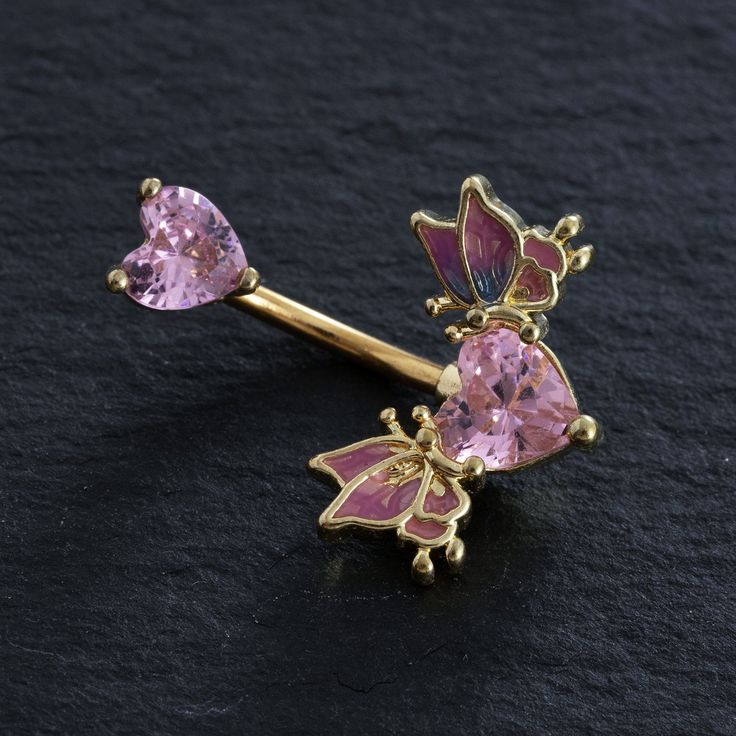 a pair of pink and gold earrings with butterflies on them, sitting on a black surface