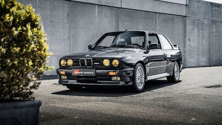 a black bmw is parked in front of a building with concrete walls and potted plants