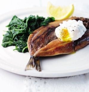 a white plate topped with fish, greens and poached eggs on top of it