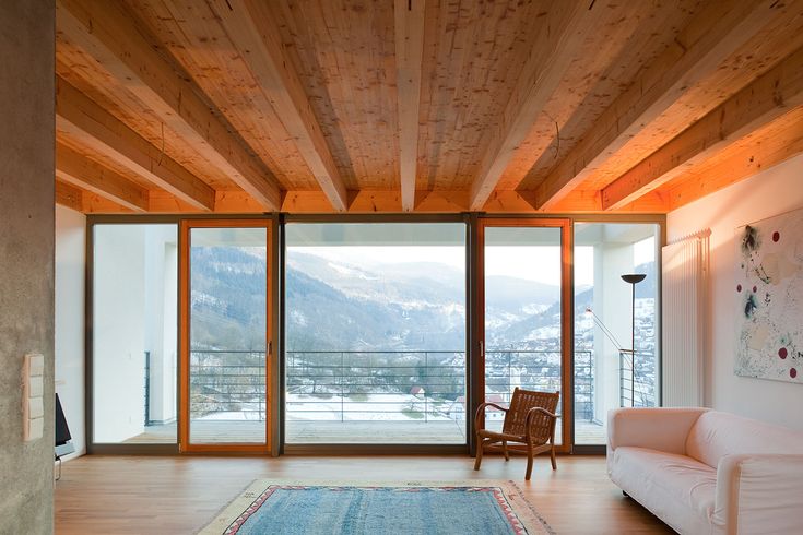 a living room filled with furniture and large windows next to a wooden ceiling covered in wood planks