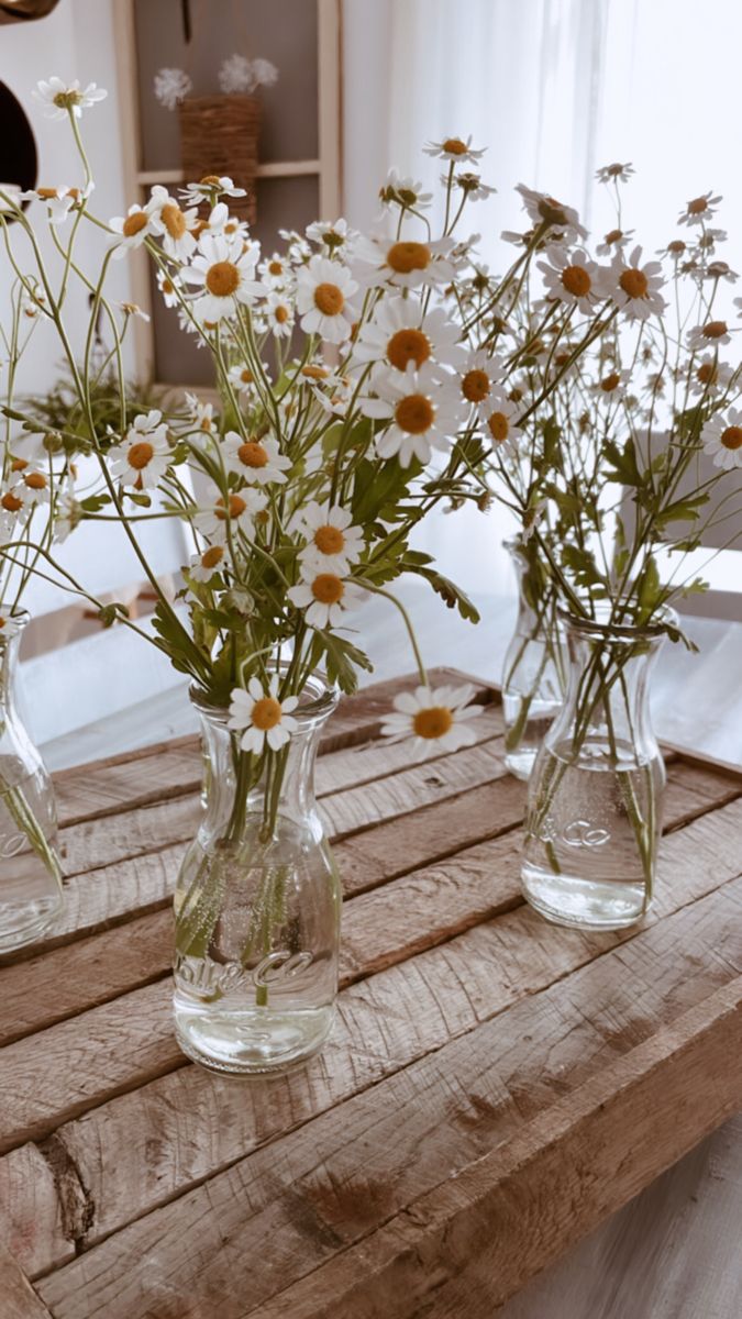 three clear vases filled with white and yellow flowers on top of a wooden table