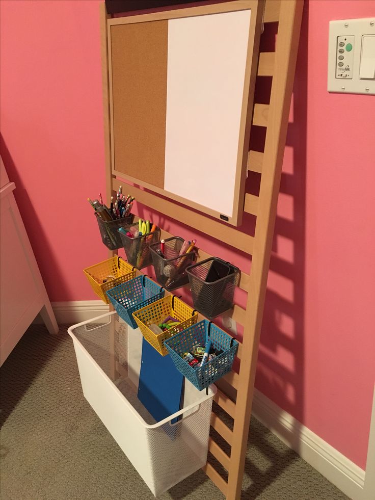 there is a ladder with baskets on it next to a white box and pink wall