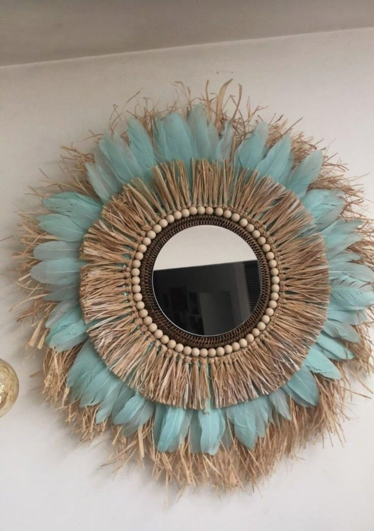 a decorative mirror hanging on the wall next to a candle and some feathers around it