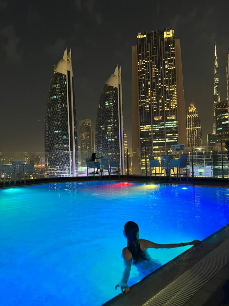 a woman sitting in the middle of a swimming pool with skyscrapers in the background