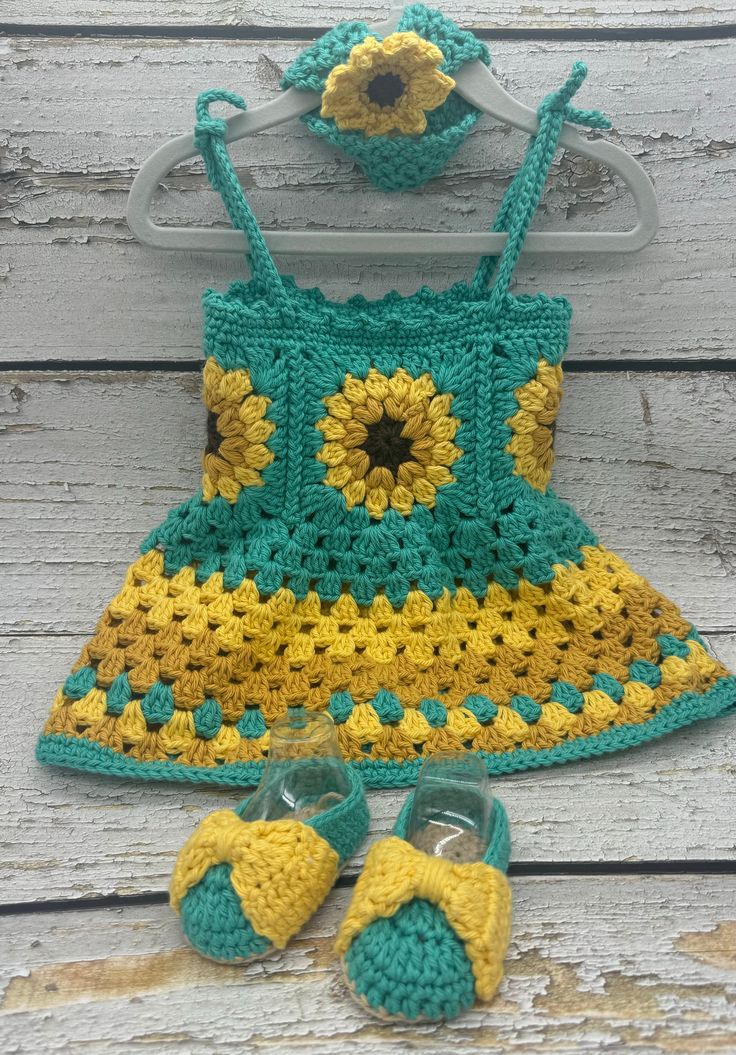 a crocheted sunflower dress and matching shoes are on the wooden floor next to a pair of baby slippers