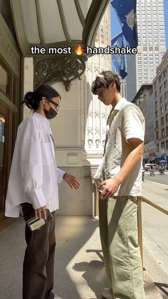 two people are standing on the sidewalk and one is holding something in his hand while the other looks at him