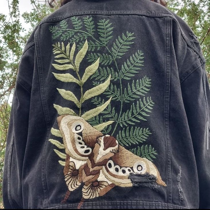 a woman wearing a jean jacket with an image of two birds on the tree branch