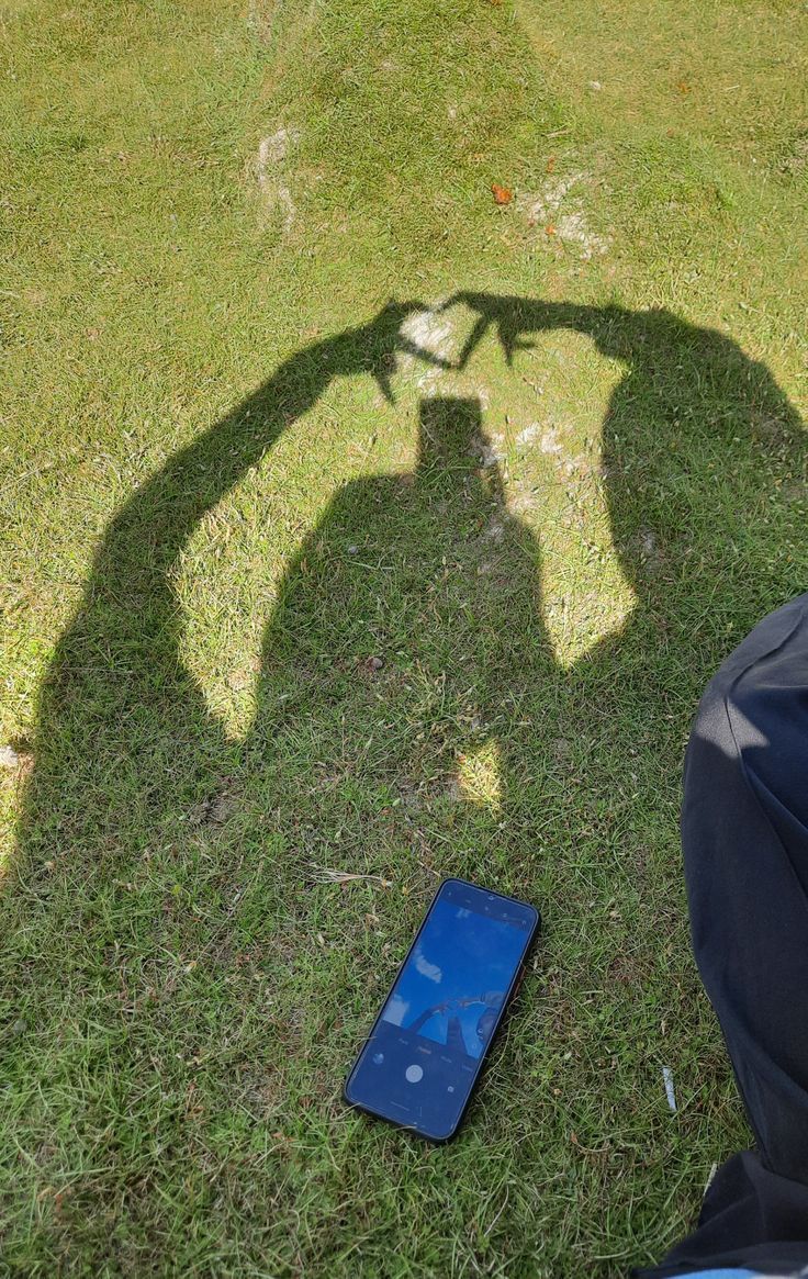 the shadow of a person standing next to a cell phone on the ground in front of them