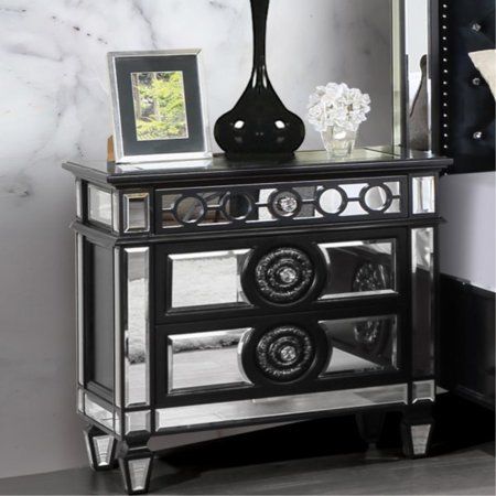 a black and silver mirrored cabinet with an ornate mirror on the top, two flowers in vases next to it