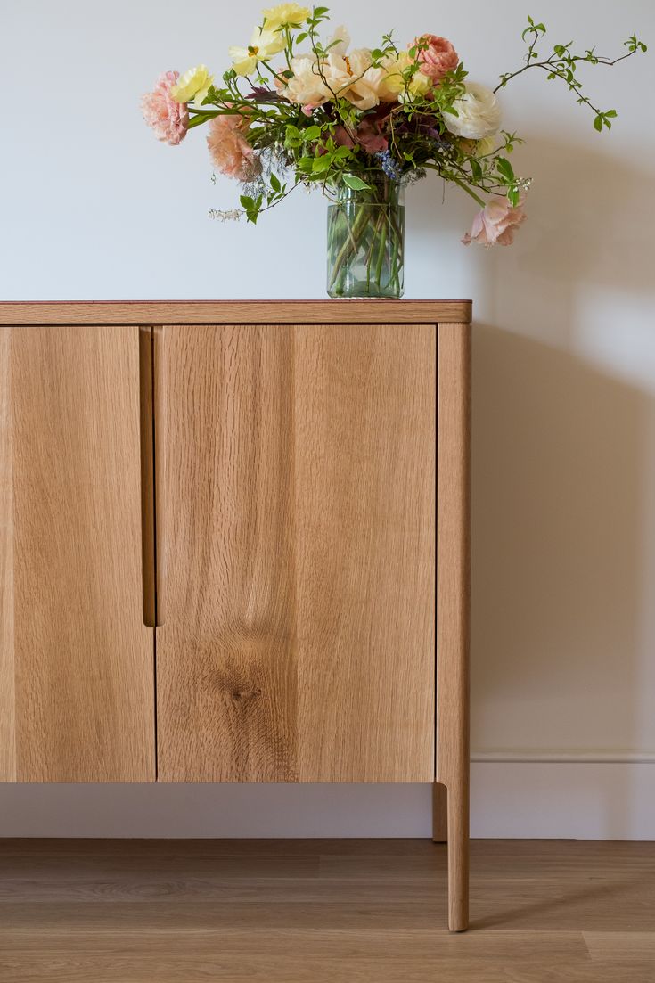 a vase filled with flowers sitting on top of a wooden cabinet next to a wall