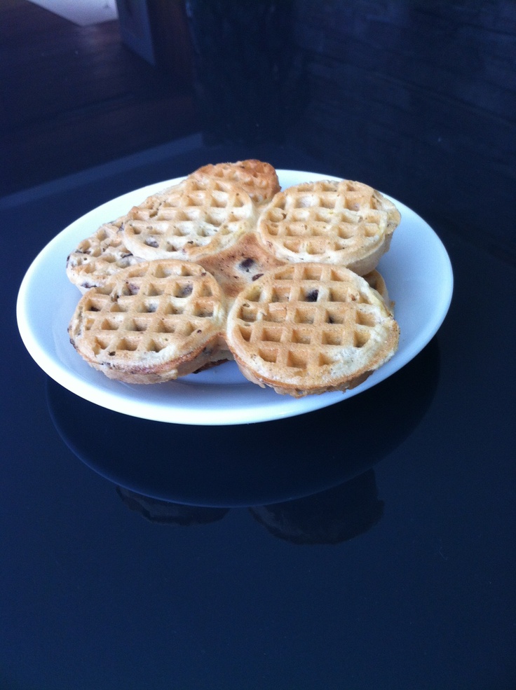 four waffles on a white plate sitting on a black table top with water in the background