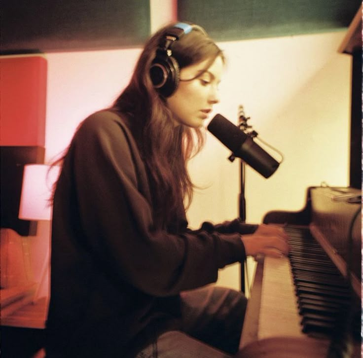 a woman with headphones sitting in front of a piano and microphone, listening to music