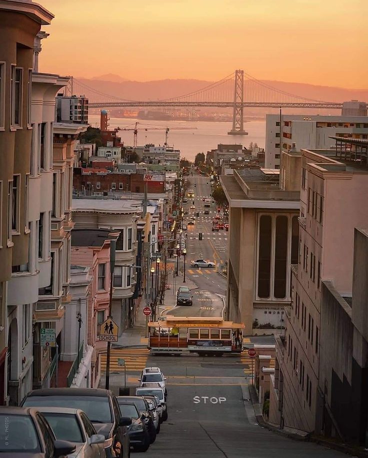 a city street with cars parked on both sides and the bay bridge in the background