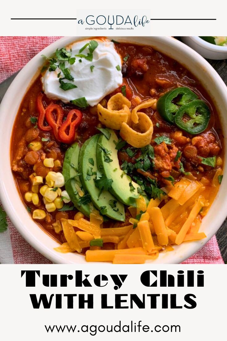 a white bowl filled with chili, cheese and avocado on top of a table