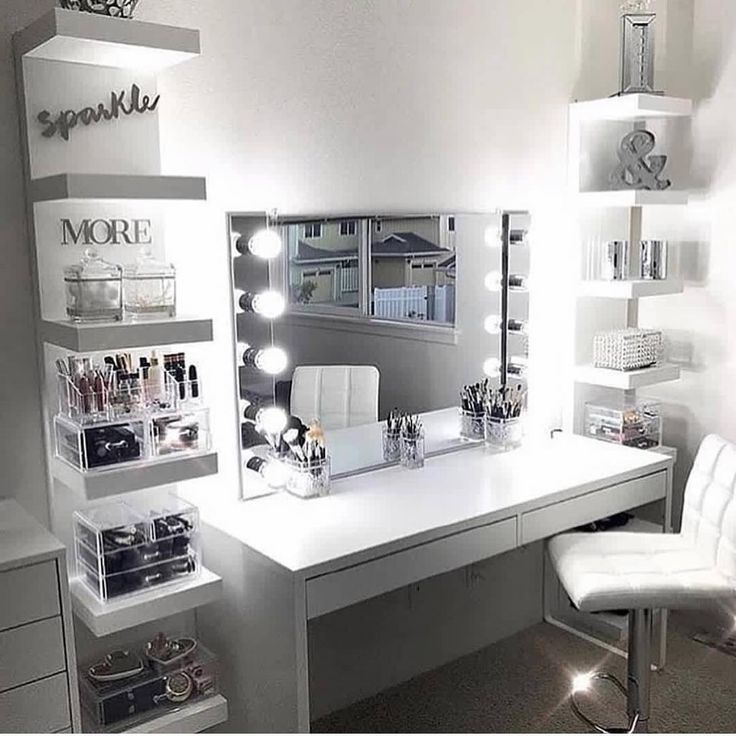 a white desk topped with lots of drawers under a mirror and lighted lights above it