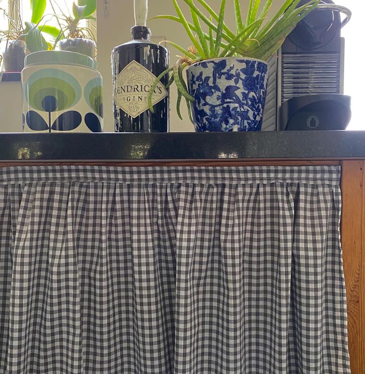 the kitchen counter is covered with gingham curtains and potted plants on top