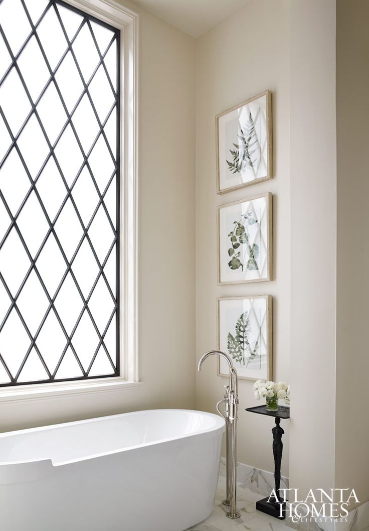 a white bath tub sitting under a window next to a wall with pictures on it