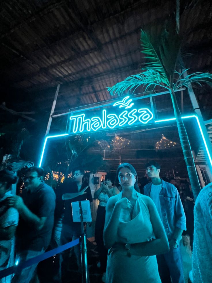 a woman standing in front of a sign that says thalasssa at night time