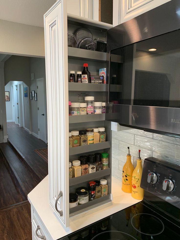 an open cabinet in the middle of a kitchen with lots of spices and condiments