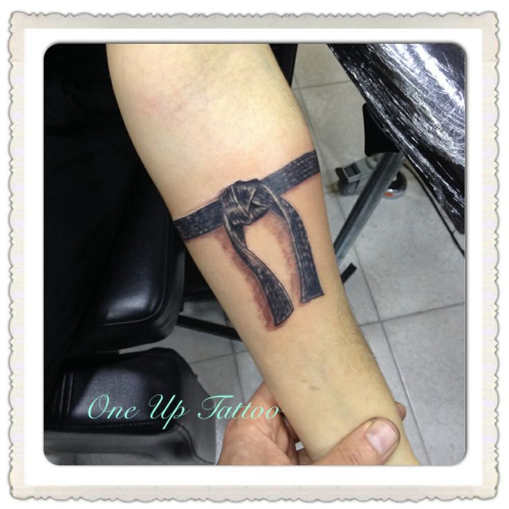 a person with a tattoo on their arm holding up a cross and ribbon in the shape of a heart