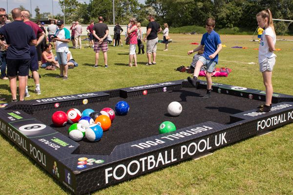 children playing pool on an inflatable table at a sports event with other people watching