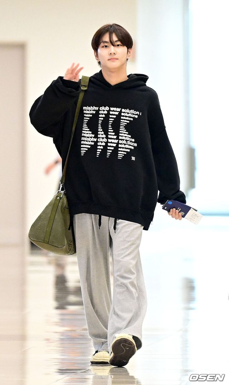 a young man walking down a runway wearing a black sweatshirt and grey pants with white writing on it