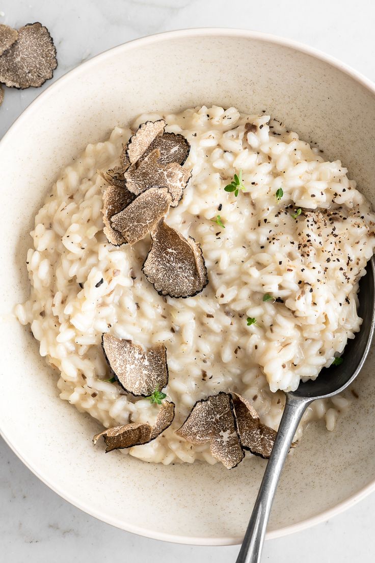 a bowl filled with rice and mushrooms on top of a white counter next to silver spoons