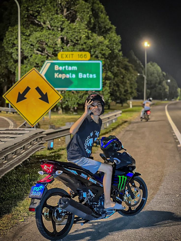 a young boy sitting on top of a motorcycle next to a street sign at night