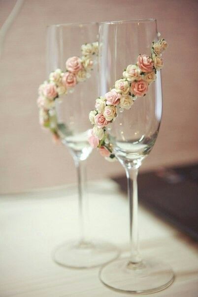 two wine glasses with flowers in them sitting on a table