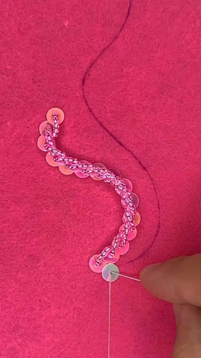 someone is making a beaded bracelet with pink thread and buttons on it, while another hand holds the string