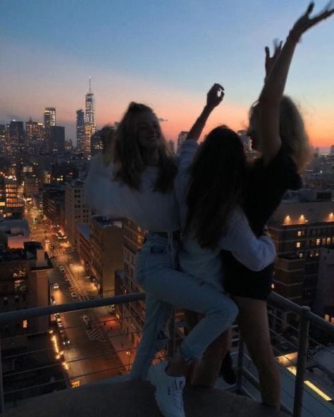 two women standing on top of a building with their arms in the air