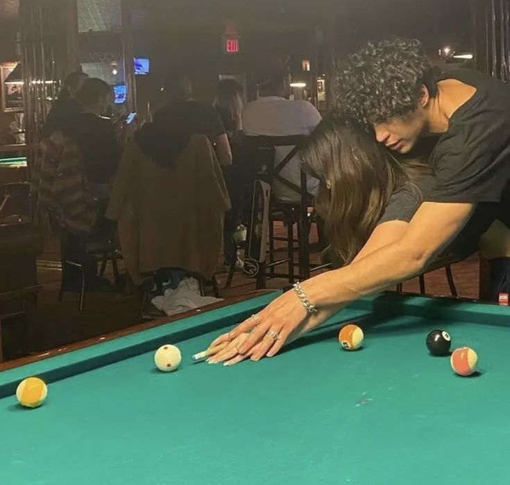 a man and woman leaning over a pool table with balls in front of them,