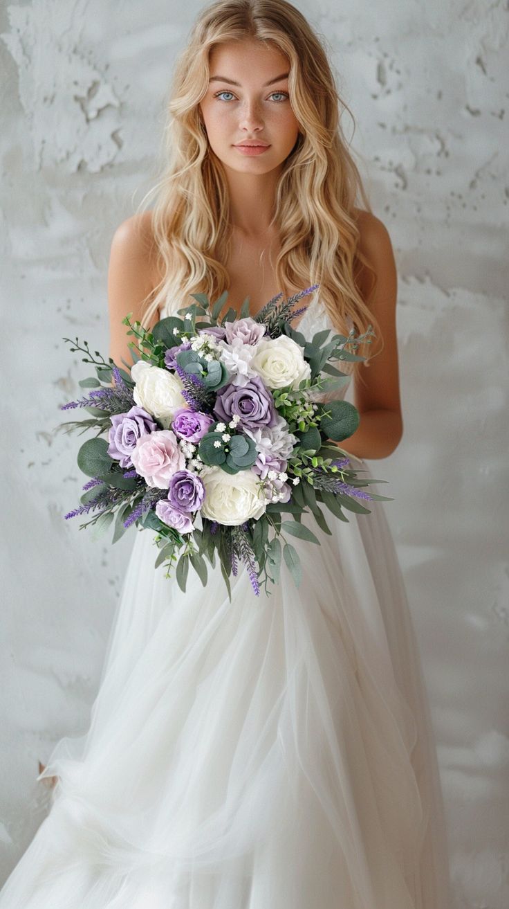 a woman in a wedding dress holding a bouquet of purple and white flowers with greenery