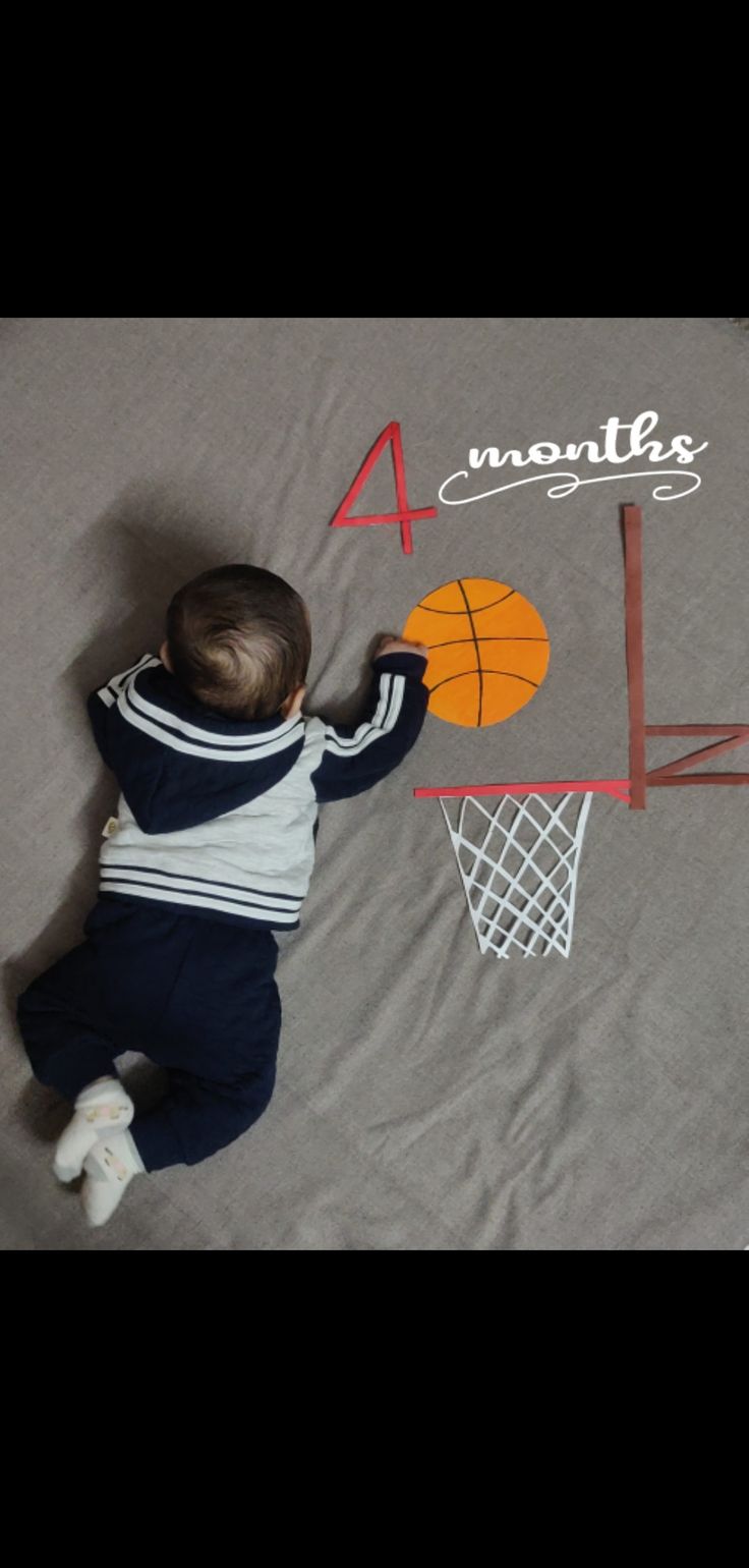 a baby laying on top of a bed next to a basketball net and number four