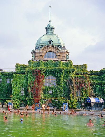 many people are swimming in the water near an old building with ivy growing on it