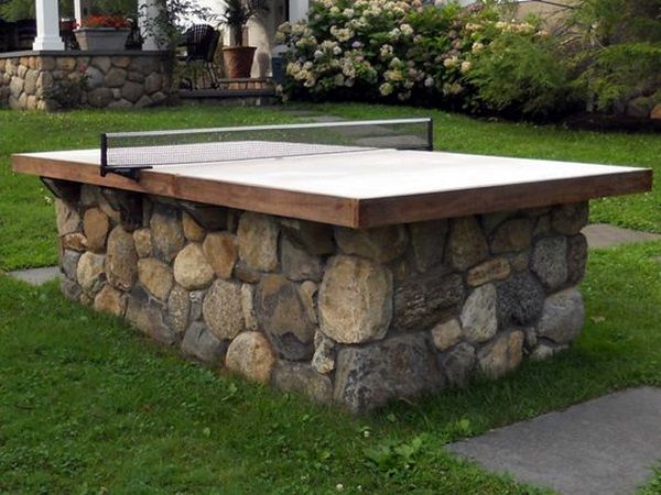 a ping pong table sitting on top of a lush green field next to a stone wall