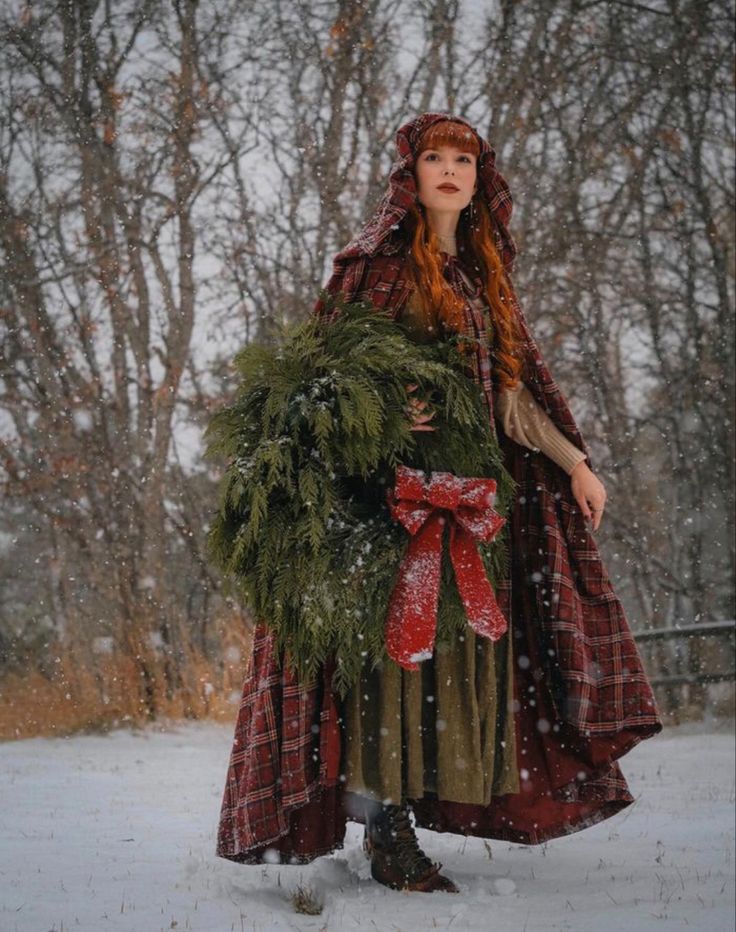 a woman dressed in red and green standing in the snow with wreaths on her head