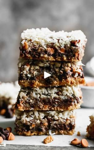 three pieces of chocolate coconut bars stacked on top of each other with nuts scattered around them