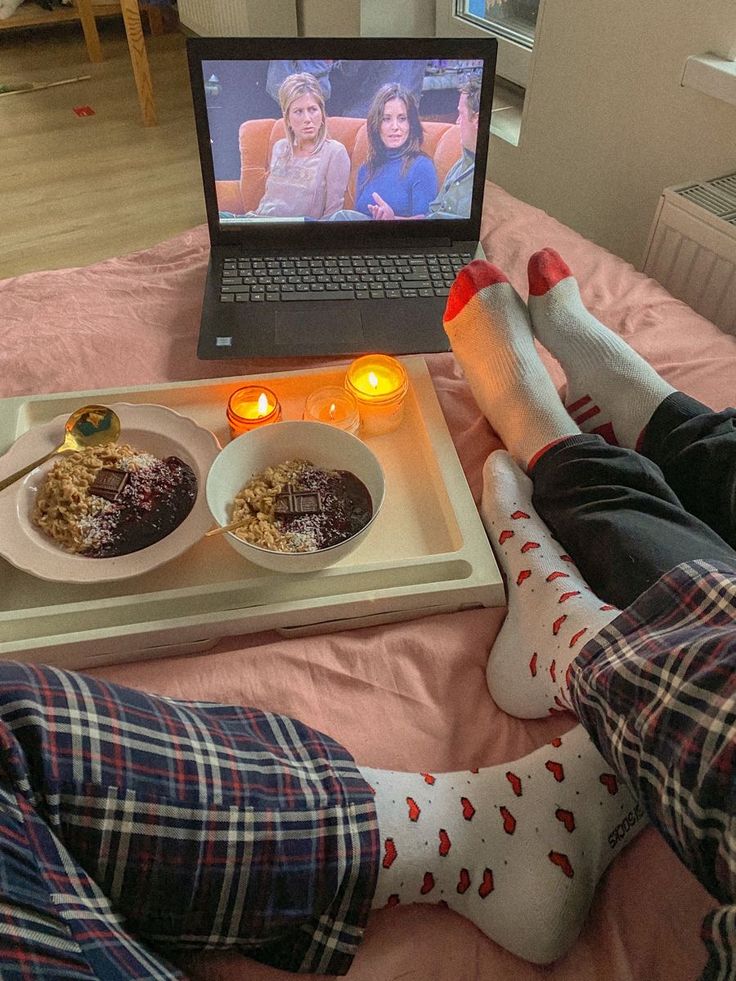 two people sitting on a bed with their feet up in front of a laptop