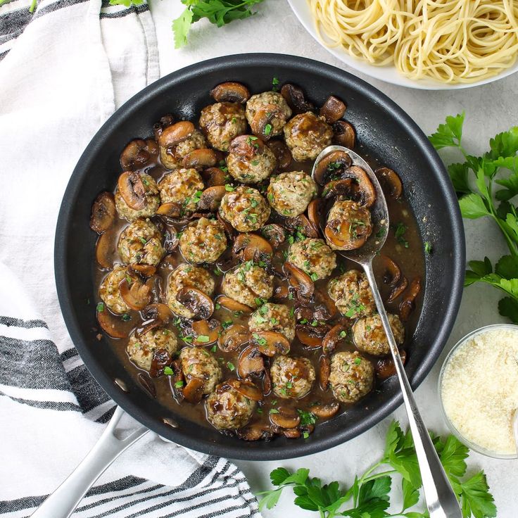 a skillet filled with meatballs and mushrooms next to some parmesan cheese