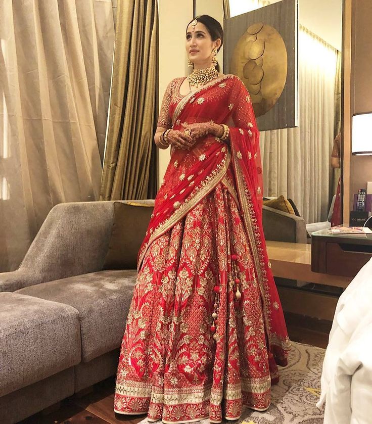 a woman in a red and gold bridal gown standing in front of a couch