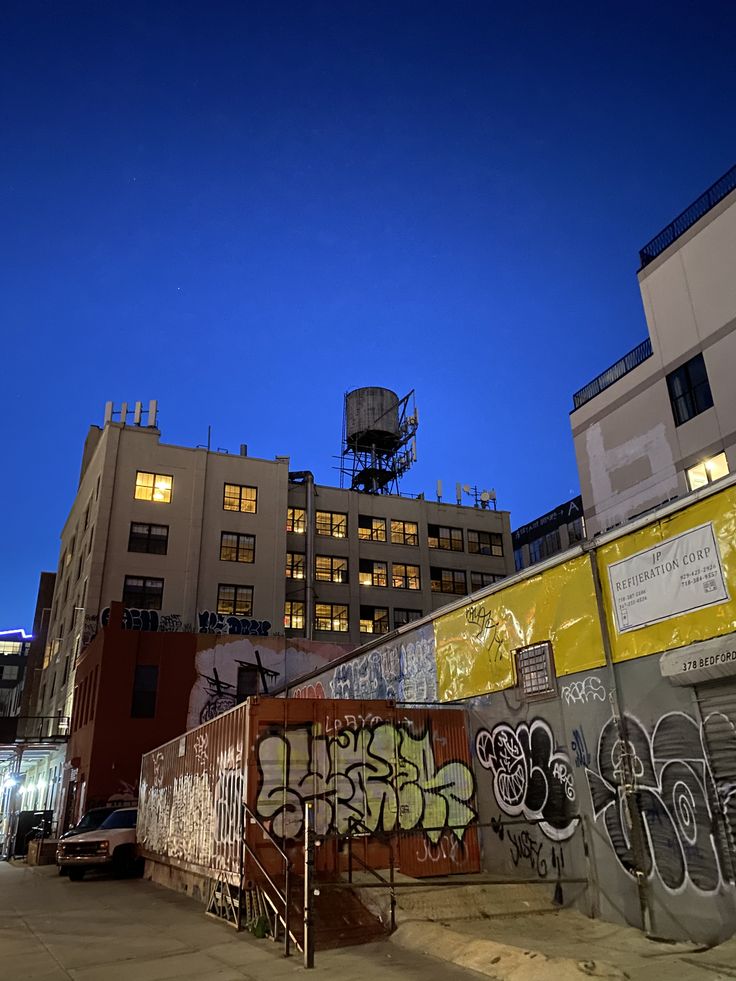 an empty parking lot with graffiti on the walls and buildings in the background at night