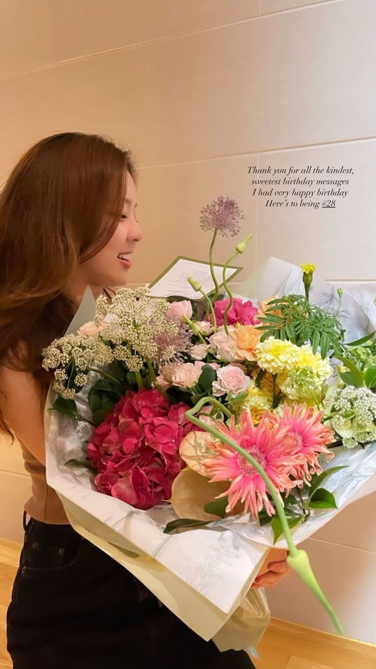 a woman holding a bouquet of flowers in her hand and looking at the wall behind her