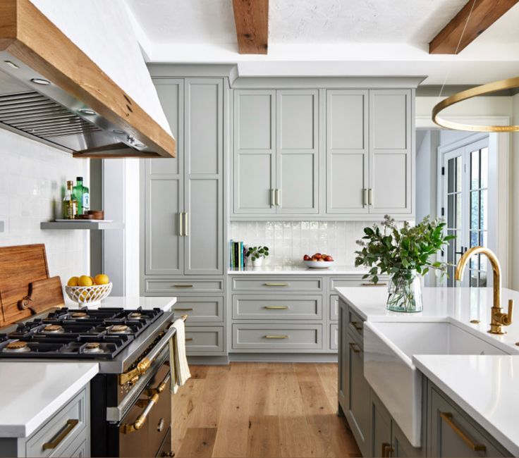 a kitchen with white counter tops and gray cabinets in the center, along with wooden flooring