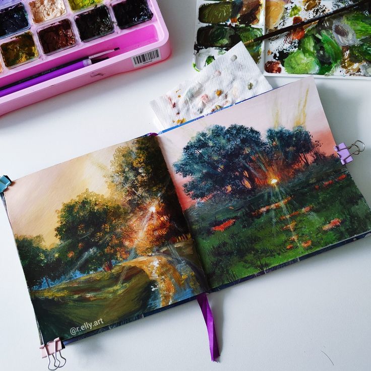 an open painting book with watercolors and paintbrushes on the table next to it