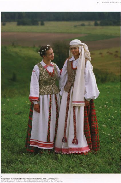 two women dressed in traditional clothing standing next to each other on a lush green field