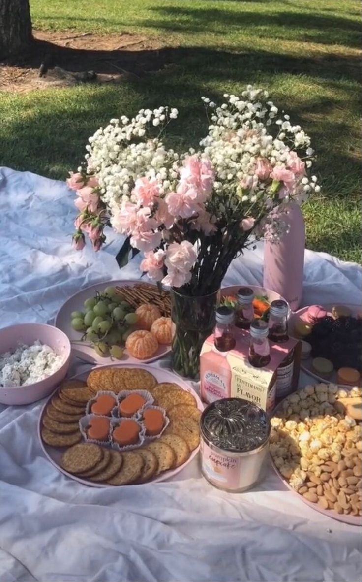 a table topped with lots of food on top of a white cloth next to a tree