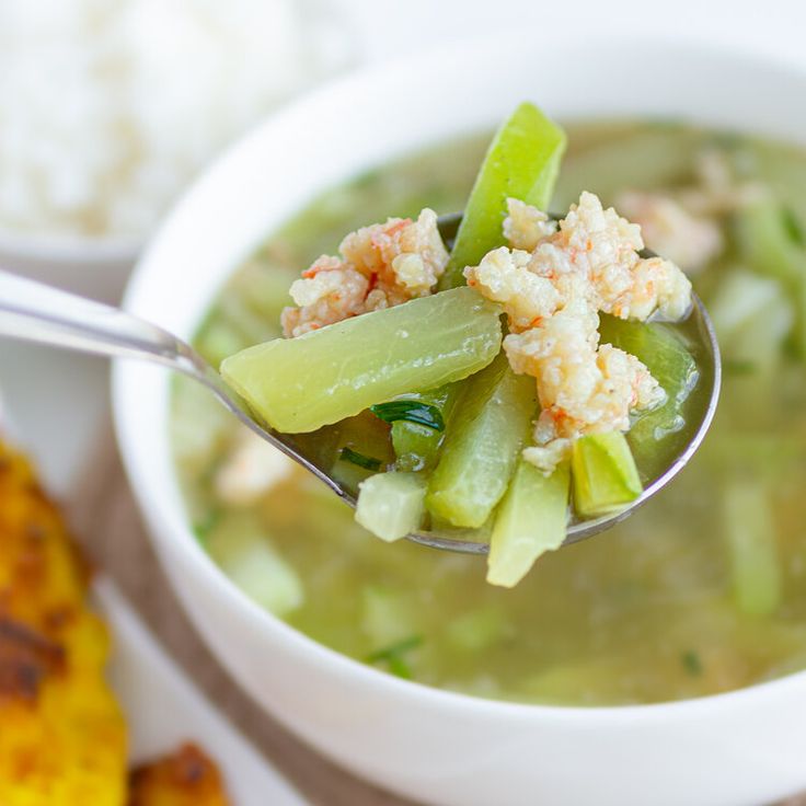 a spoon full of soup with celery and shrimp on the side next to corn