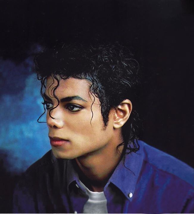 a close up of a person wearing a blue shirt and black hair with curly curls on his head