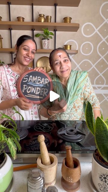 two women standing next to each other in front of a table with plants and pots on it